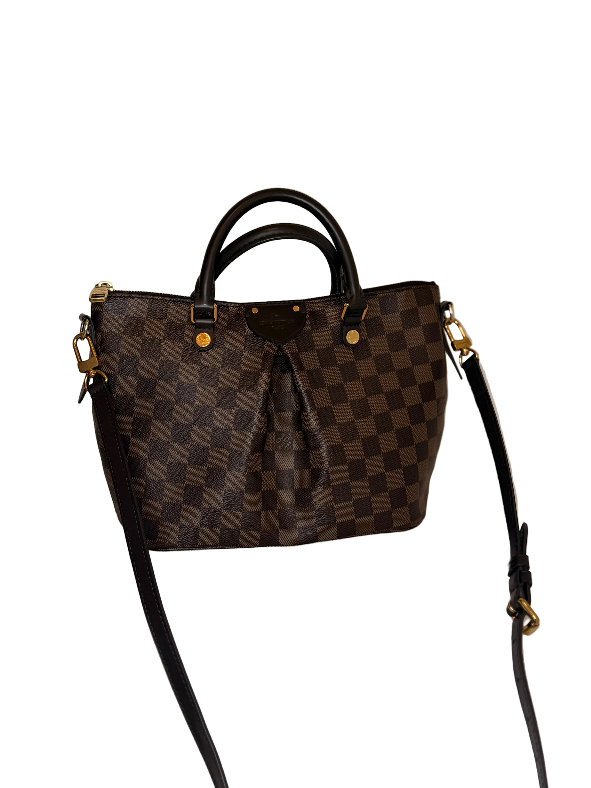 A Louis Vuitton handbag in the Damier Ebene checkered pattern, featuring dark brown and black checkered squares, black leather handles and shoulder strap, and gold-tone hardware, displayed on a light beige textured surface against a neutral beige background.