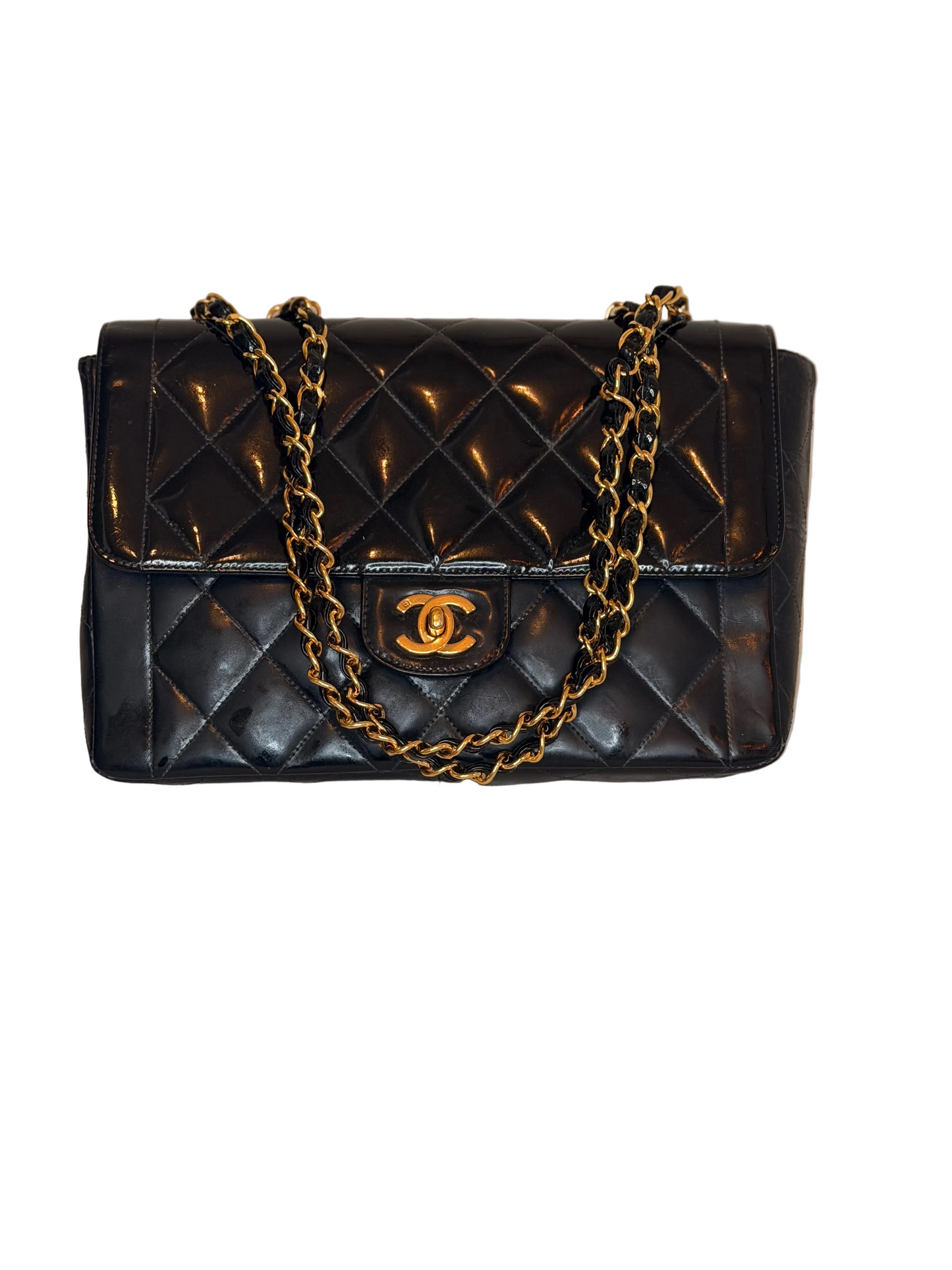 A black quilted leather handbag with a gold-tone chain strap and a gold interlocking CC logo on the front, displayed on a light beige textured surface against a neutral beige background.