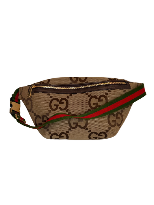A Gucci monogram canvas waist bag with a green and red web stripe, displayed on a light-colored fabric surface against a plain light background.